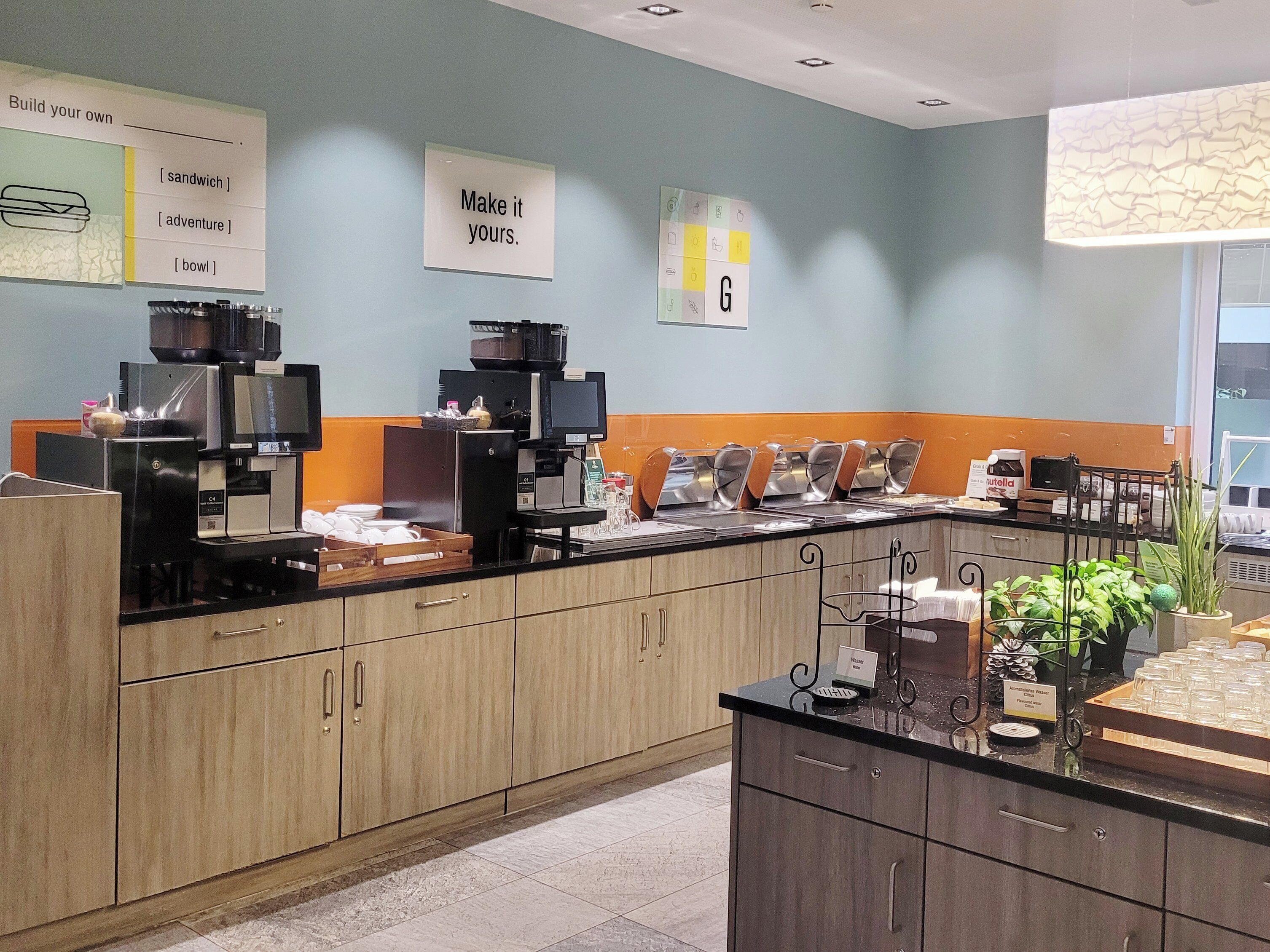 Un área de cocina moderna con estación de café, presentación tipo buffet y un cartel que dice “Make it yours.”