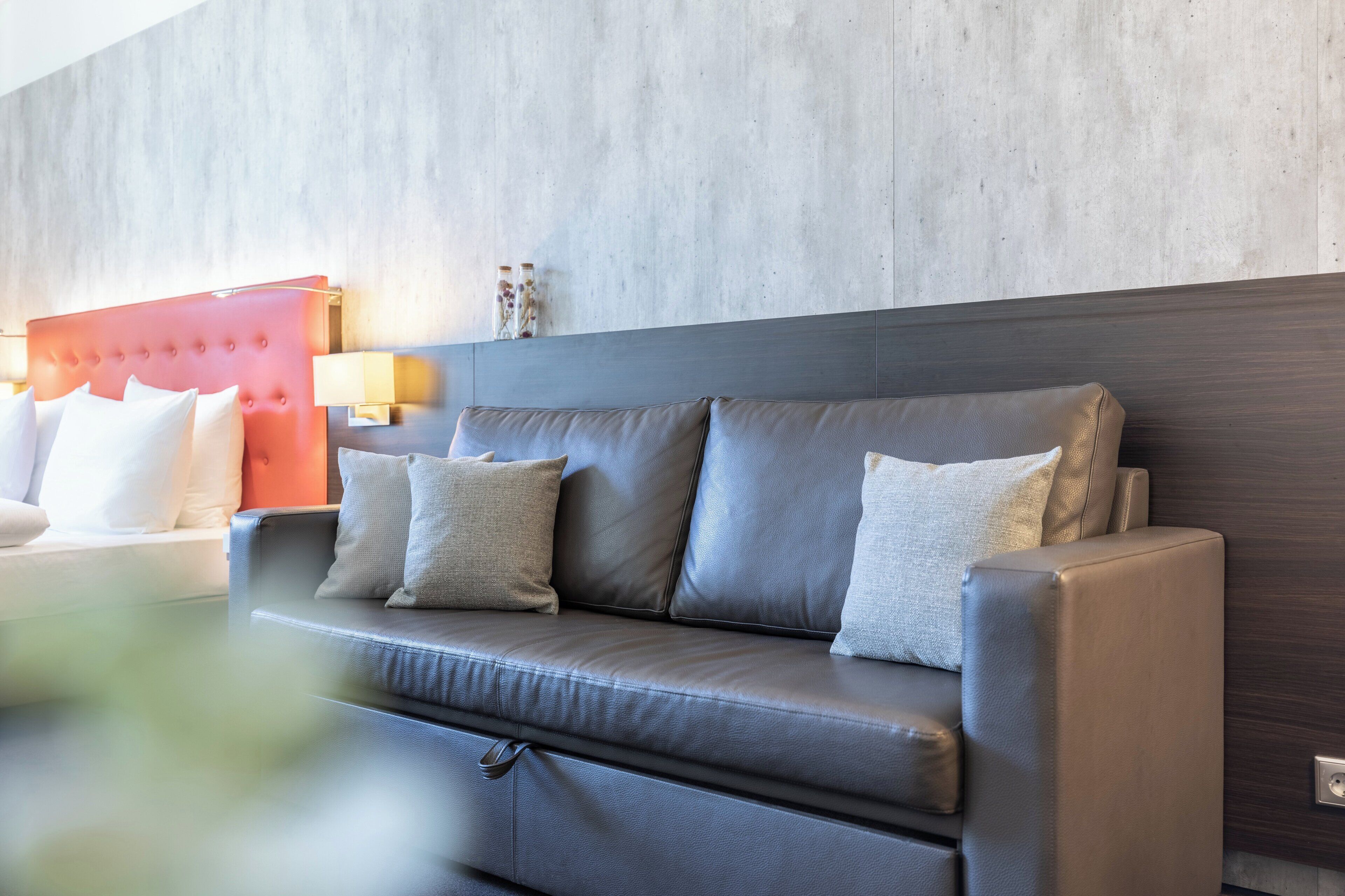 Habitación de hotel moderna con sofá de cuero gris, cabecera roja y pared de hormigón.
