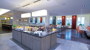 Ein moderner Hotel-Speisebereich mit einer zentralen Buffetinsel, verschiedenen Sitzgelegenheiten und großen Fenstern mit Blick.