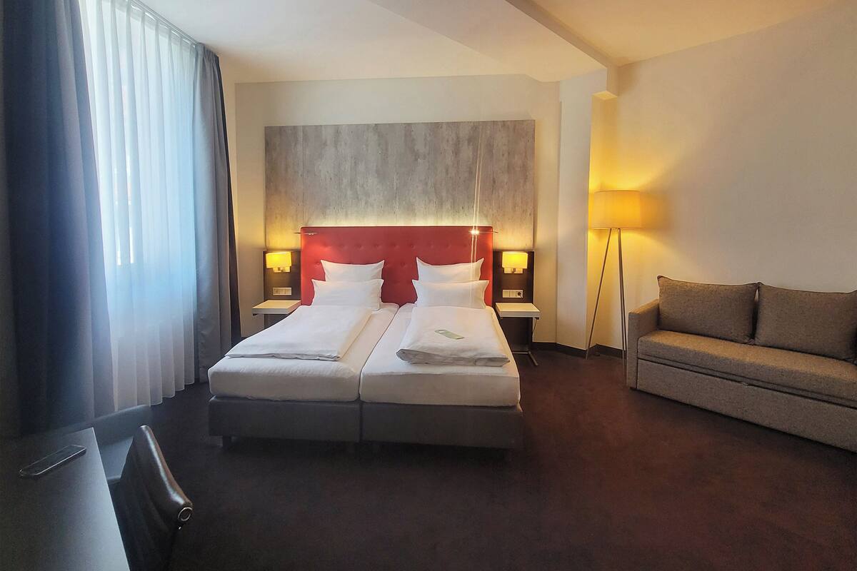 Une chambre d’hôtel avec un grand lit, deux tables de chevet avec des lampes, un canapé et un bureau avec une chaise.