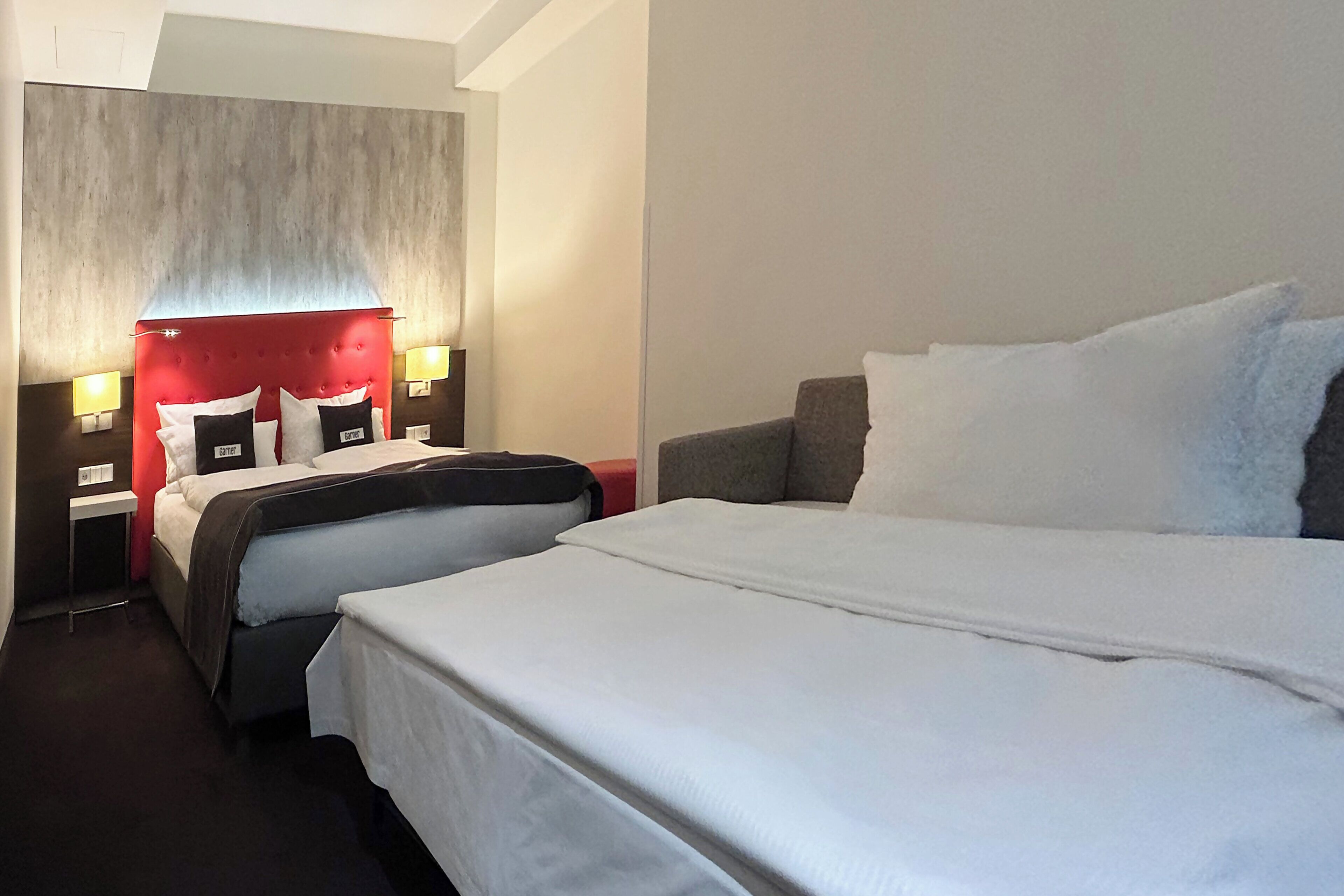 Una habitación de hotel con dos camas, un cabecero rojo y lámparas de noche.