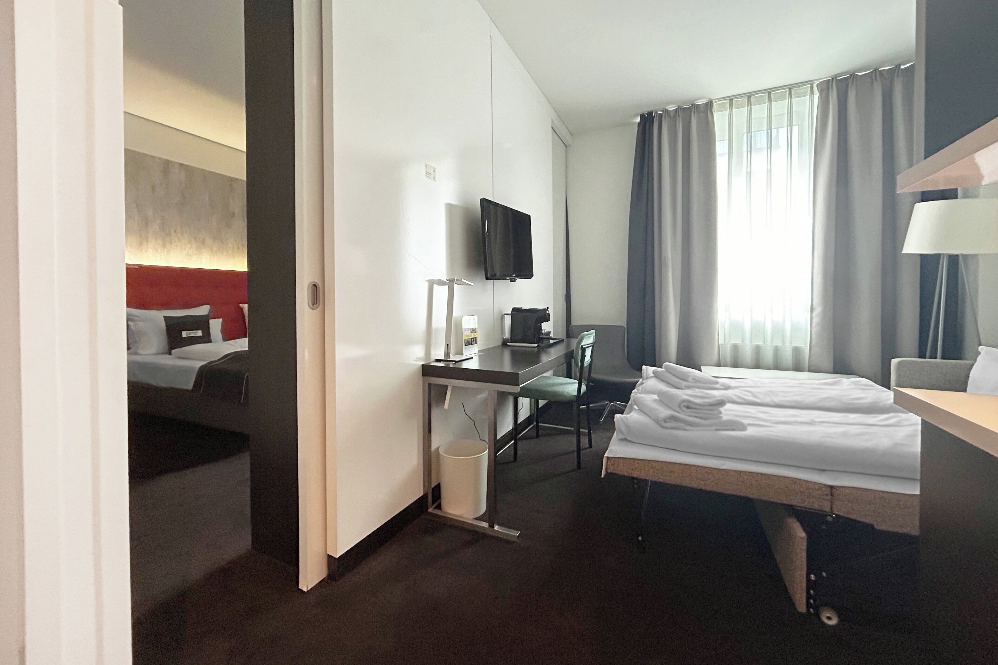 A hotel room with a bed, desk, chair, TV, and a window with curtains.