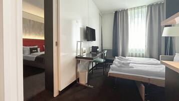 A hotel room with a bed, desk, chair, TV, and a window with curtains.