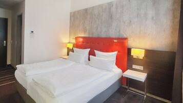 Ein Doppelbett mit weißer Bettwäsche, ein roter Kopfteil, zwei Nachttischlampen und ein kleiner Nachttisch.