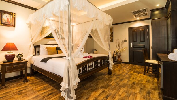 A four-poster canopy bed with a wooden frame and white bedding, a nightstand with a red lamp, and a dark wooden wardrobe. - Tanawan Phuket Hotel (Patong)