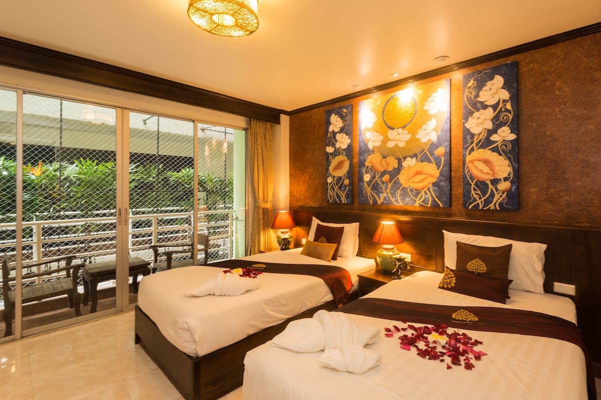 A hotel room with two beds, a balcony with a view of greenery, and artwork on the wall.