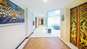 A hallway with a large traditional mural on the left, a glass partition on the right, and a tiled floor. - Tanawan Phuket Hotel (Patong)