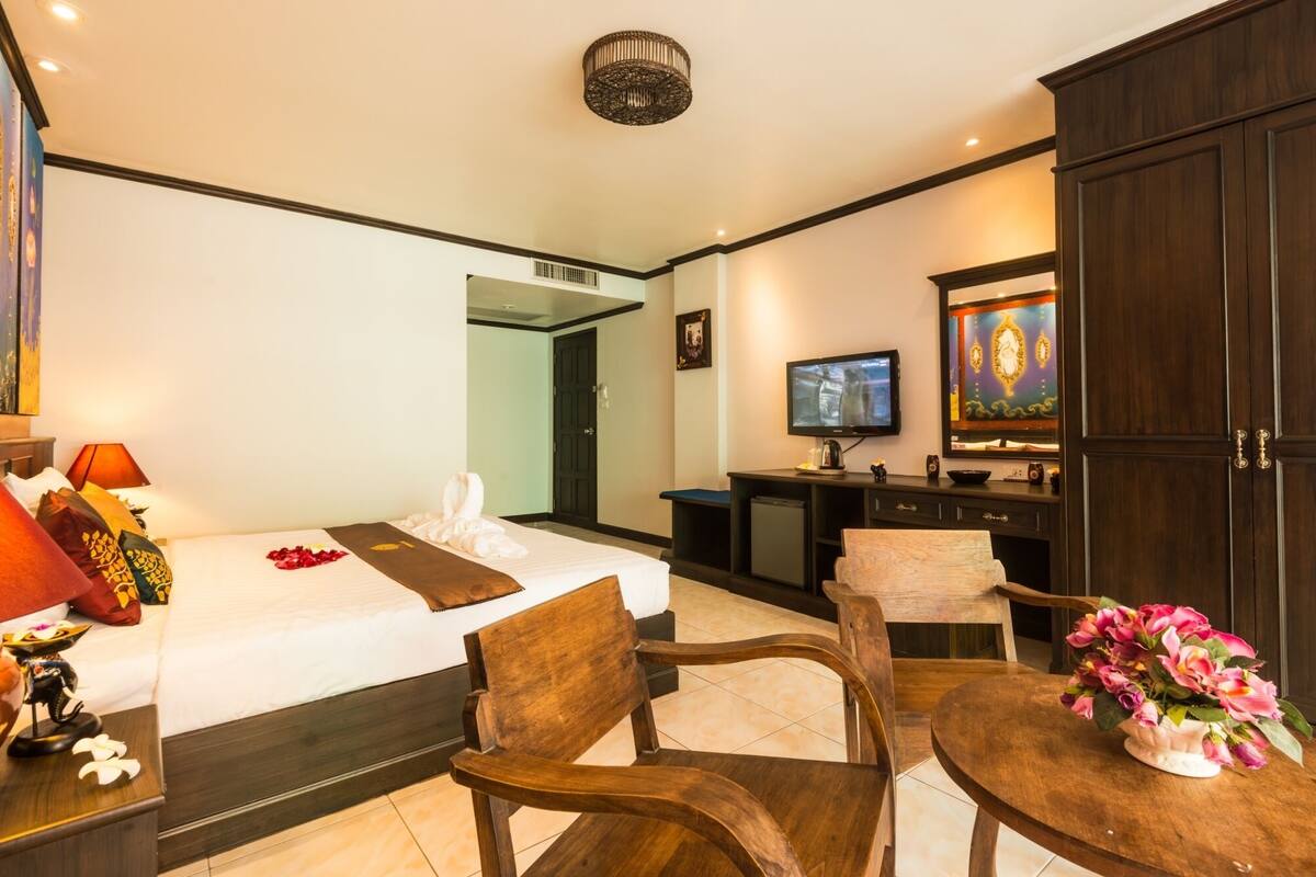 A hotel room with a bed, two wooden chairs, a small table with flowers, a TV, and a cabinet.