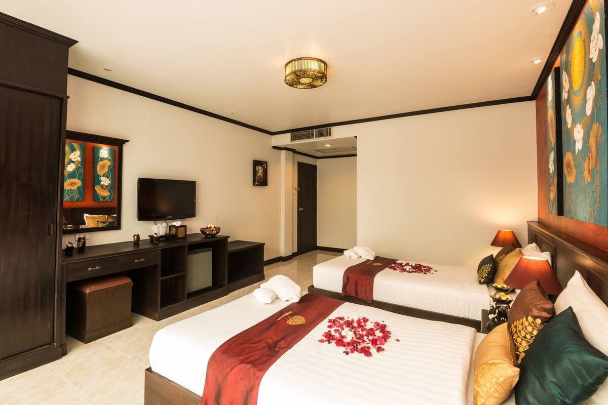 A hotel room with two beds, a desk, a television, and artwork on the walls.