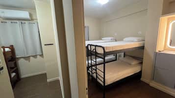 A dormitory room with bunk beds, a wooden ladder, a white air conditioning unit, and a small window with a light fixture.