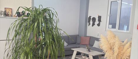 Una sala de estar moderna con un sofá gris, una mesa de centro, una planta grande en maceta y un jarrón decorativo con plumas de pampa.