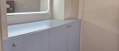 A room with a built-in wardrobe, a mirror with a light, and a wooden floor.