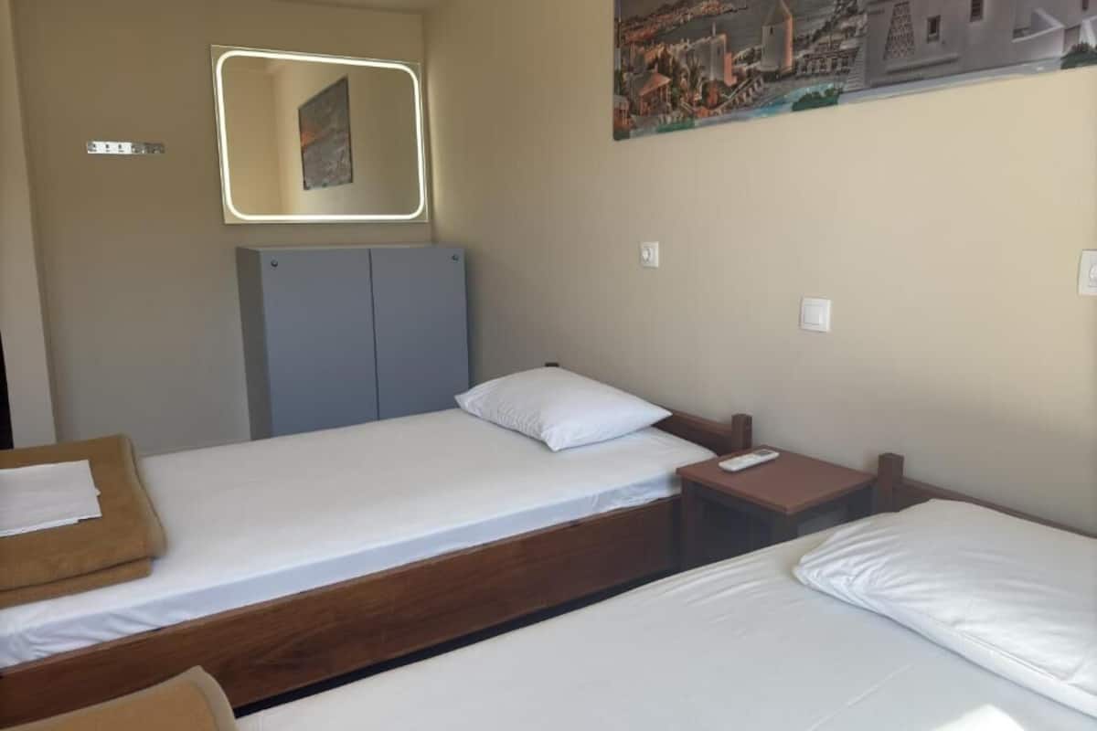 A hotel room with two beds, a wooden headboard, a nightstand, a painting on the wall, and a mirror with a light.