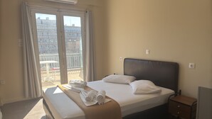 A hotel room with a bed, a nightstand, a window with curtains, and an air conditioning unit. - Paloma (Athens)