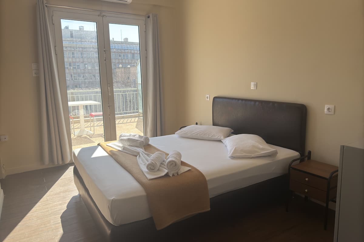 A hotel room with a bed, a nightstand, a window with curtains, and an air conditioning unit.