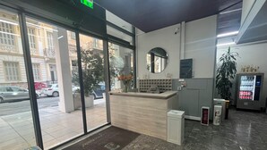A reception area with a counter, a mirror, a vending machine, and a door leading outside. - Paloma (Athens)