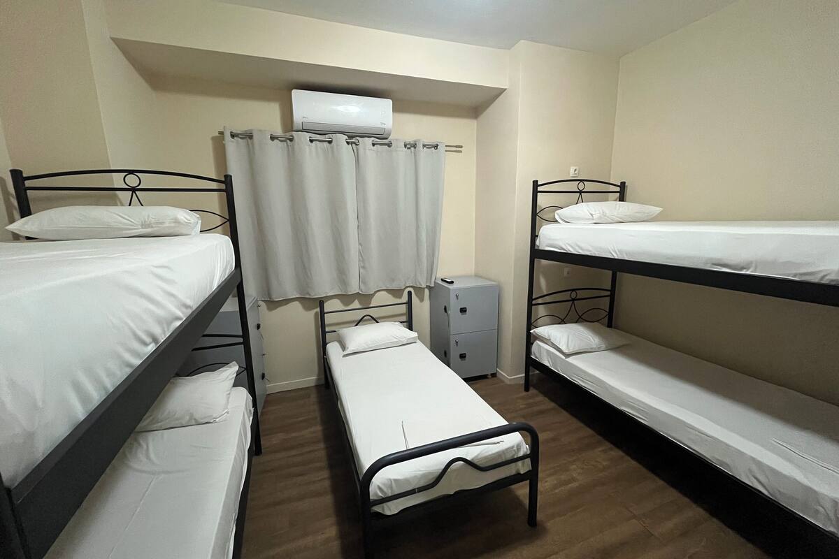 A dormitory room with bunk beds, a small bedside table, a heater, and a curtain.