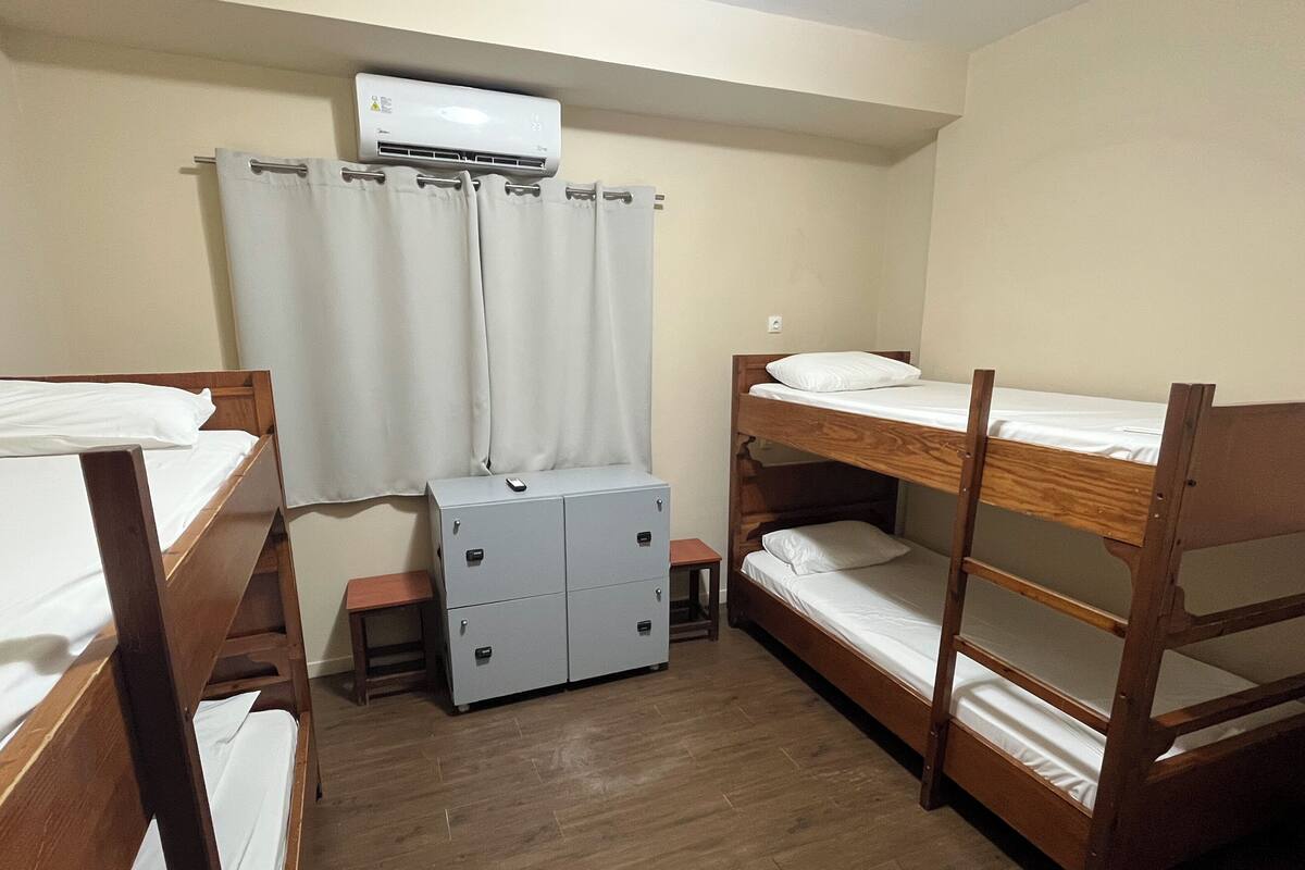 A dormitory room with bunk beds, a small desk, a cabinet, and an air conditioning unit.