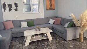A modern living room with a grey sectional sofa, a wooden coffee table, and a stone-patterned floor. - Paloma (Athens)