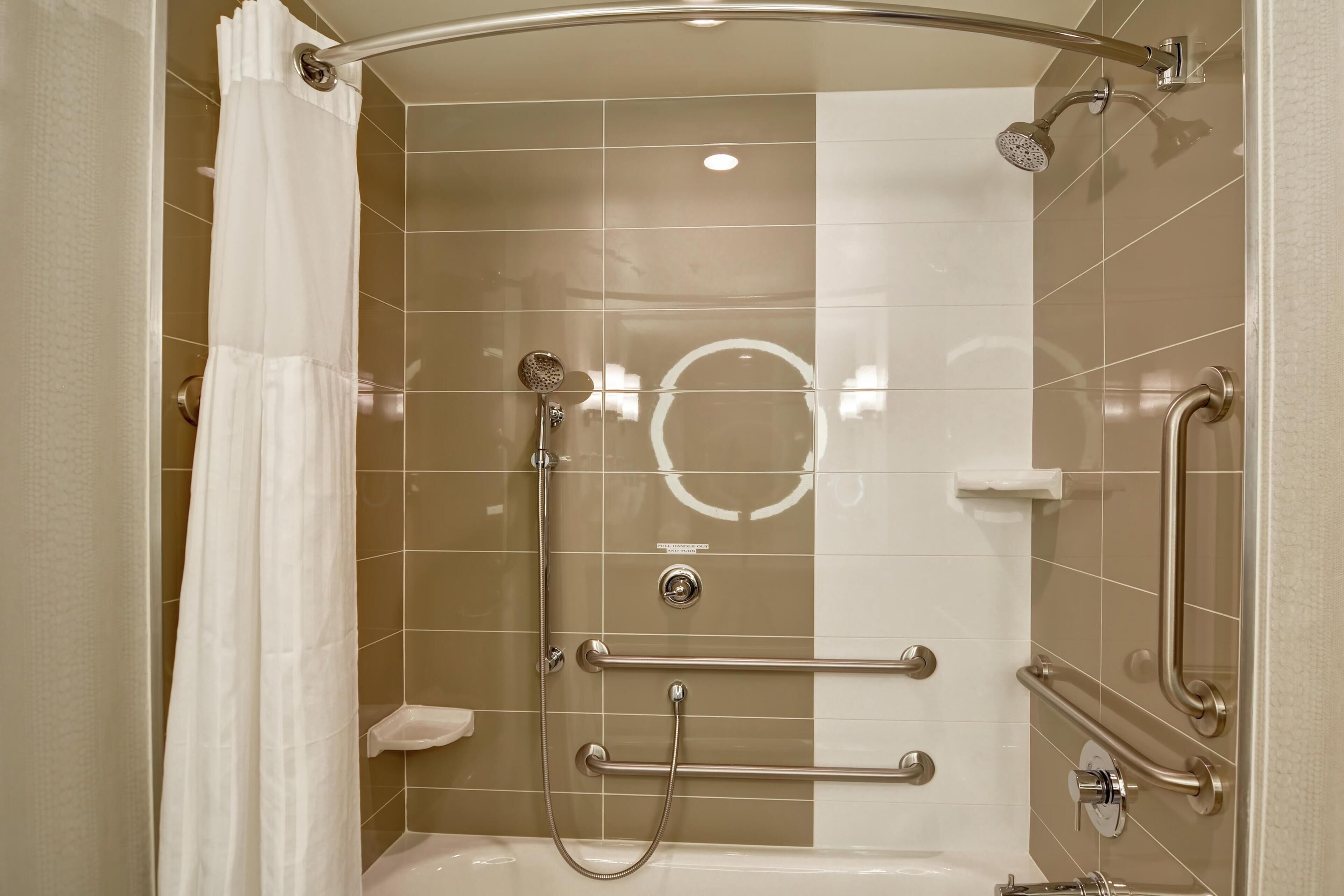 A shower with a curved glass door, grab bars, a handheld showerhead, and a handheld shower attachment.