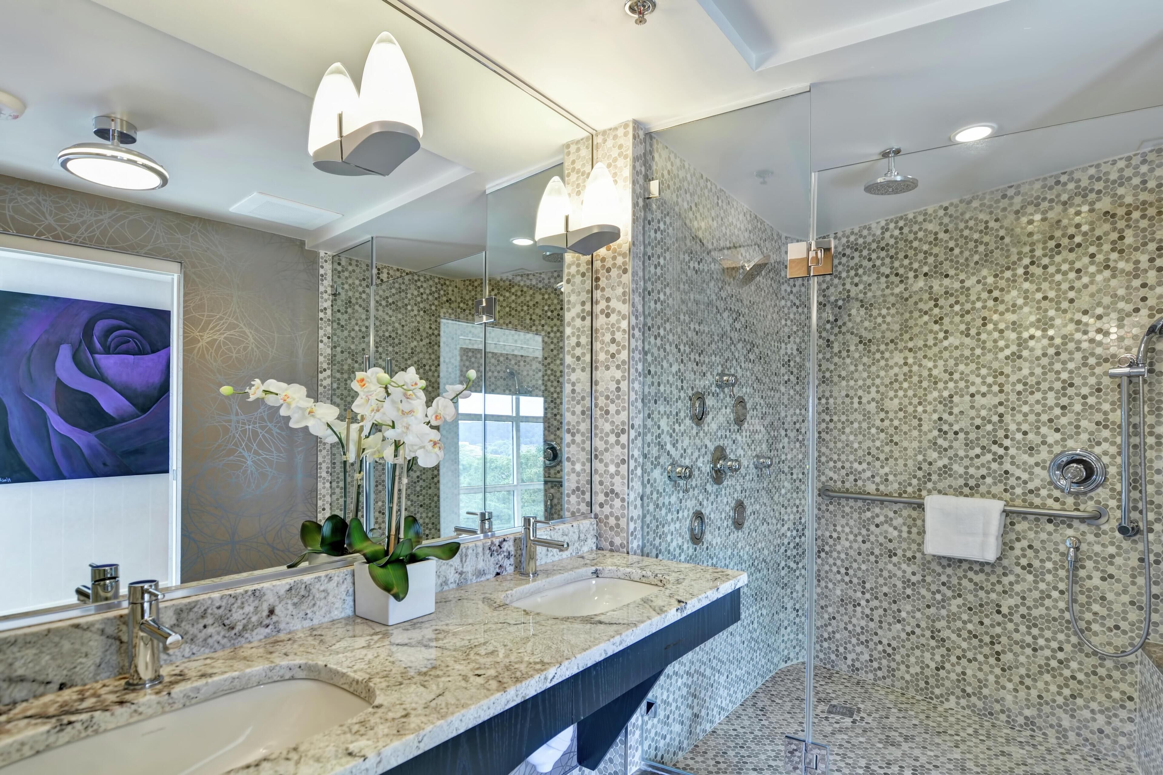 A modern bathroom with a double sink, a large mirror, and a shower with a mosaic wall.