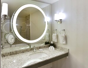 A bathroom with a round mirror, a sink, a towel rack, and a shower area.