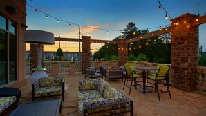 Eine Terrasse im Freien mit Steinböden, gelb-grauem Mustersofas, einem runden Tisch und Lichterketten.