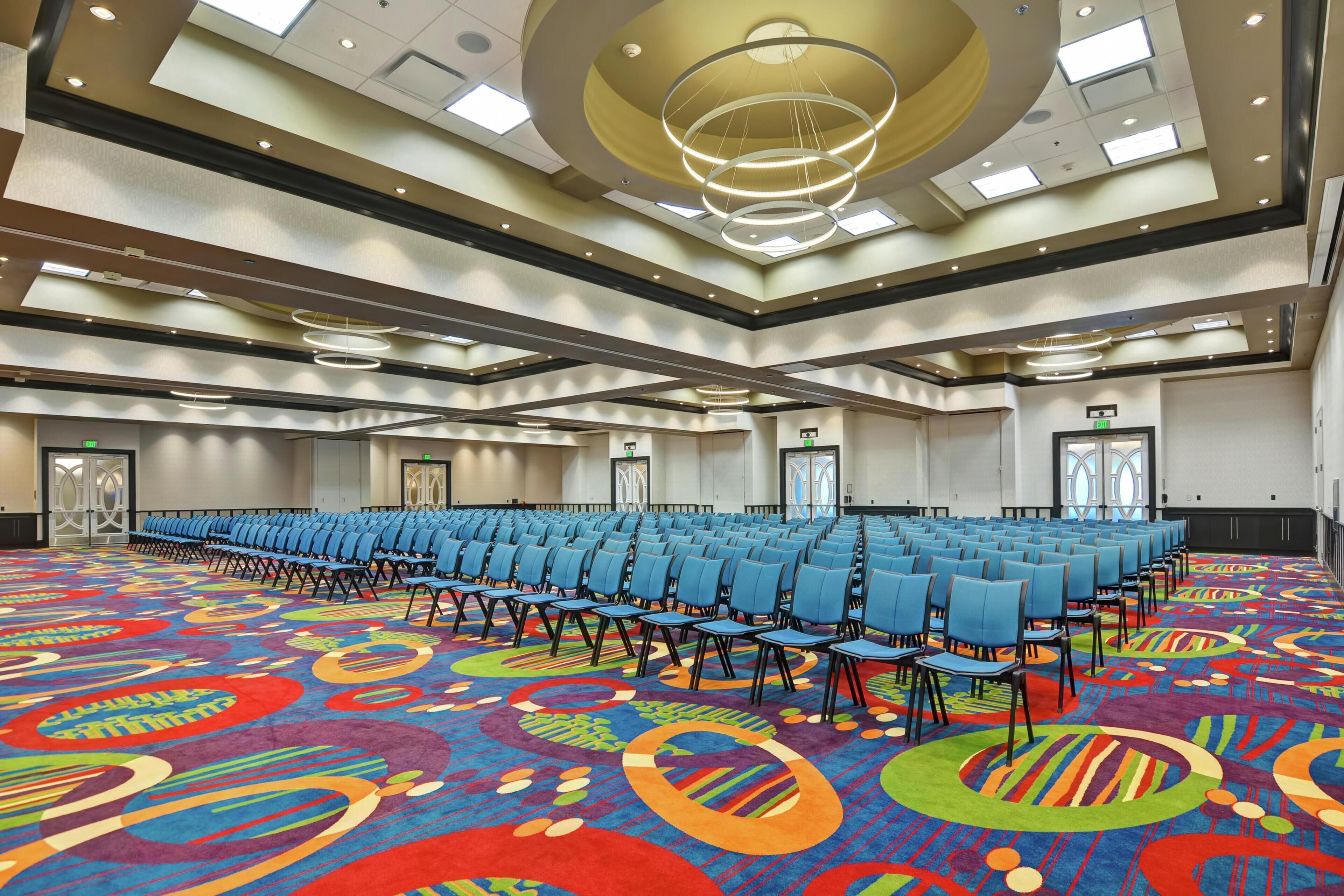 A large conference room with rows of blue chairs, a colorful carpet, and a modern ceiling design.