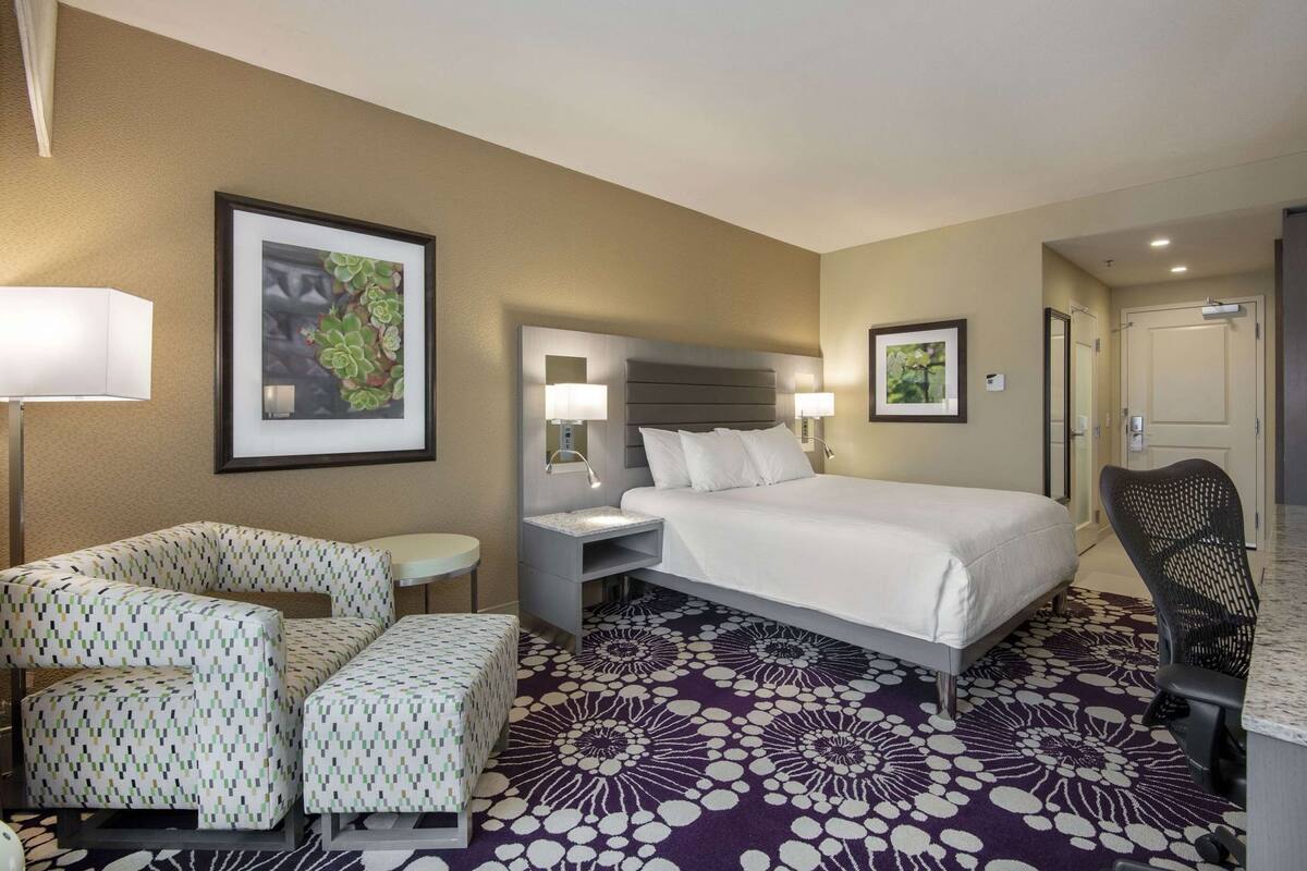 A hotel room with a bed, two chairs, a desk, and a nightstand.
