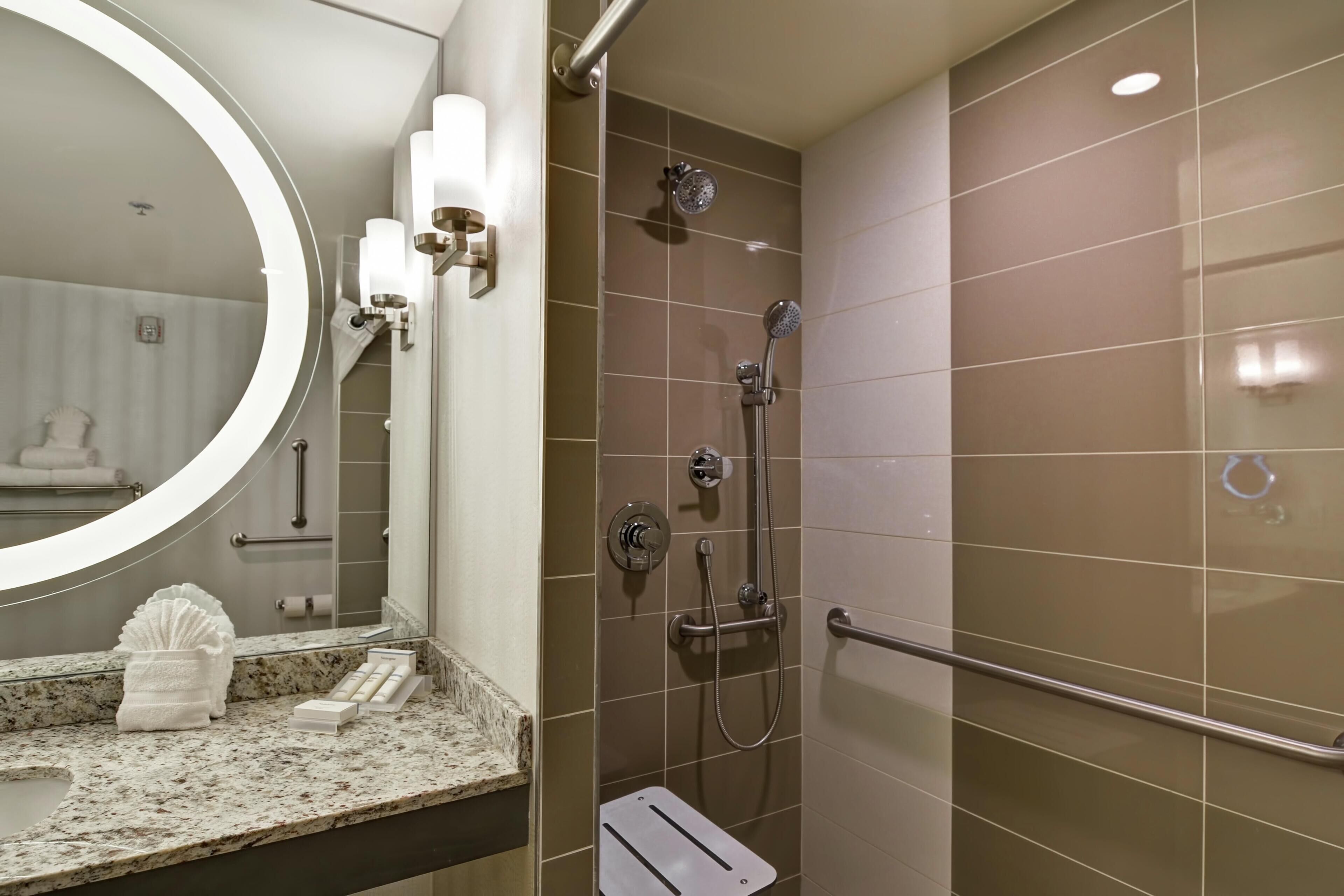 A bathroom with a round mirror, a towel rack, a shower with a handheld showerhead, and a grab bar.