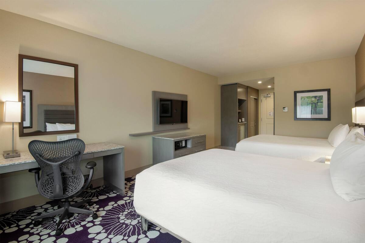 A hotel room with a bed, a desk with a chair, a television, and a mirror.