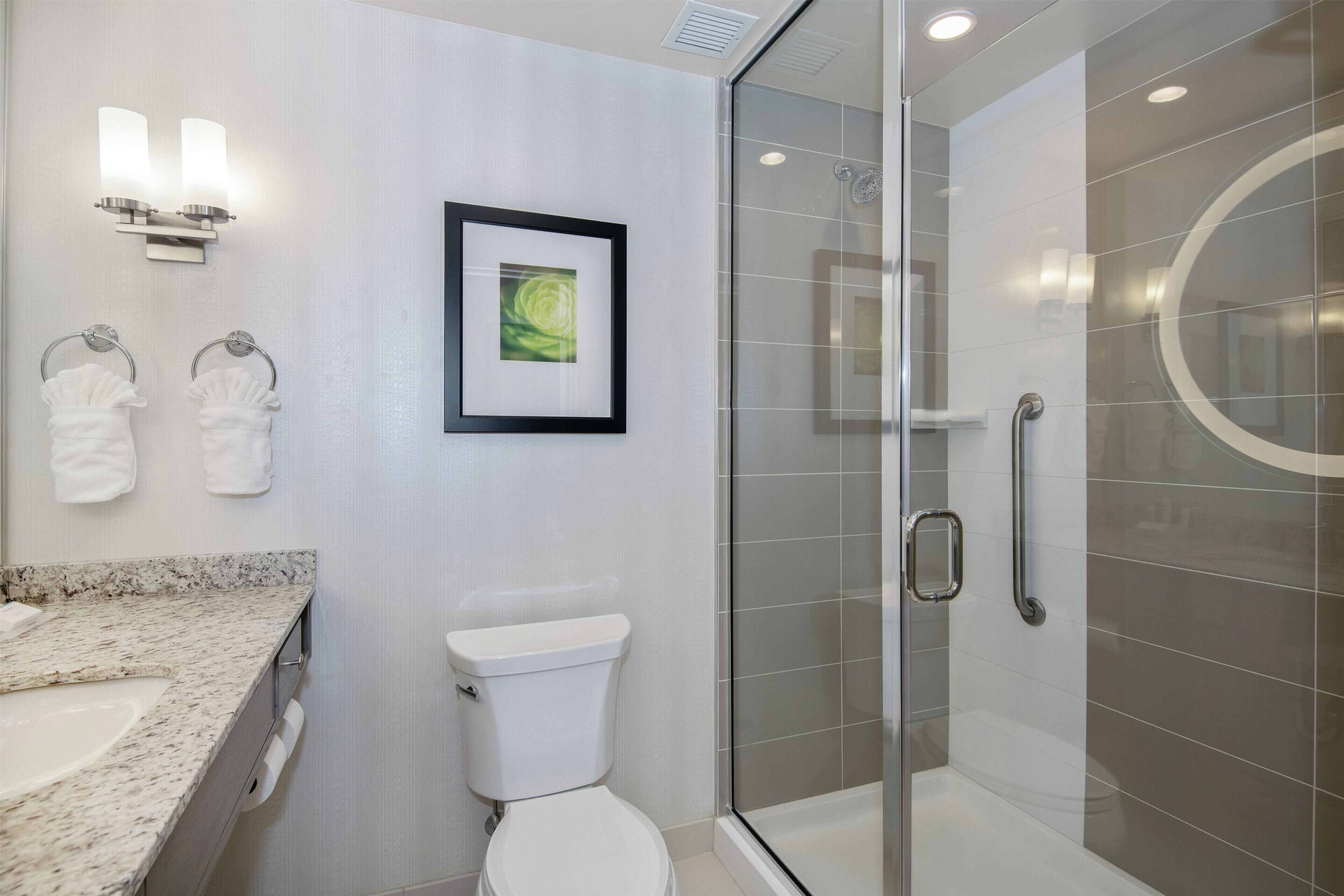 A modern bathroom with a glass-enclosed shower, a white toilet, a marble countertop, and two wall-mounted towel rings.