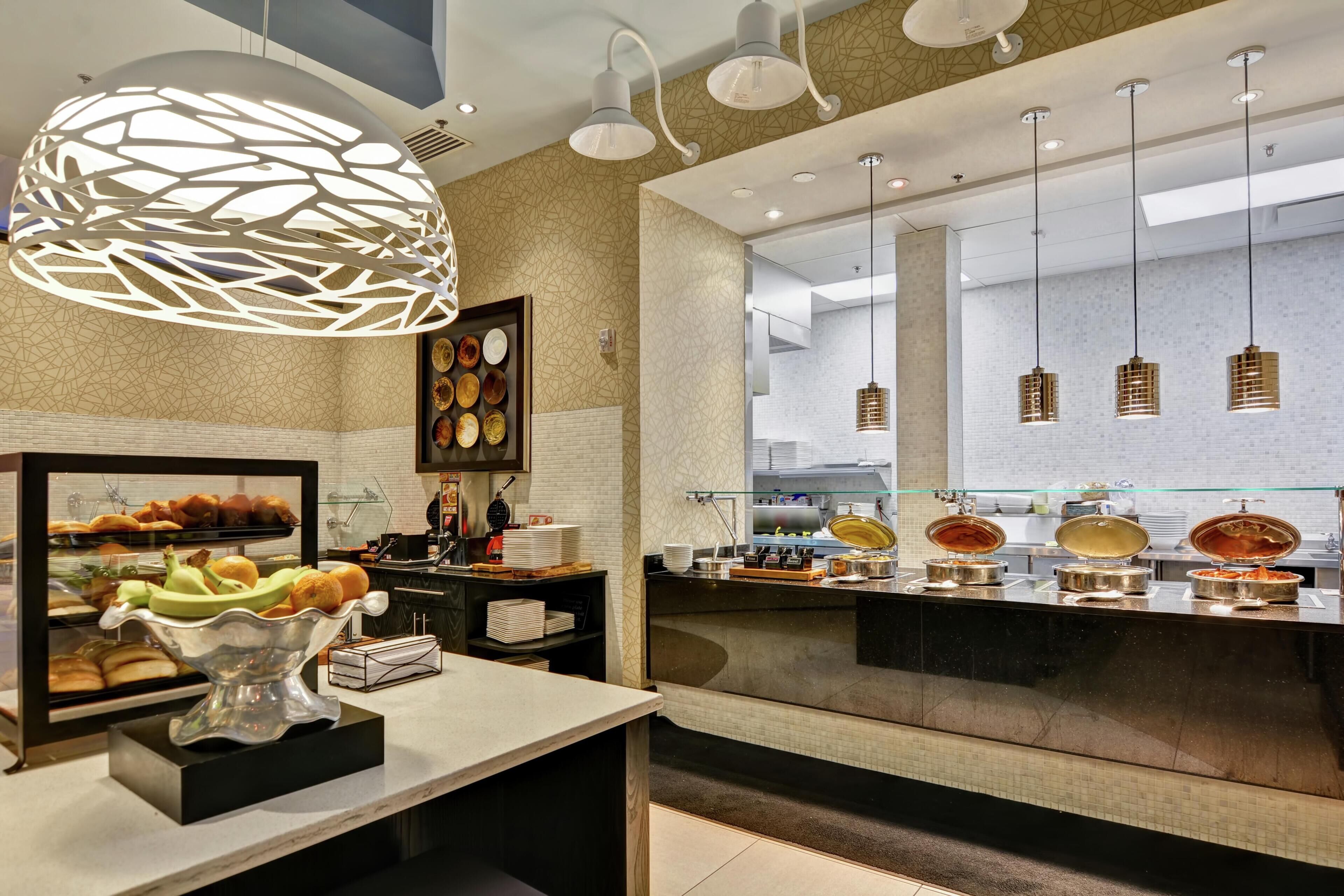 A modern breakfast bar with a variety of food options, a decorative light fixture, and a view of the kitchen area.