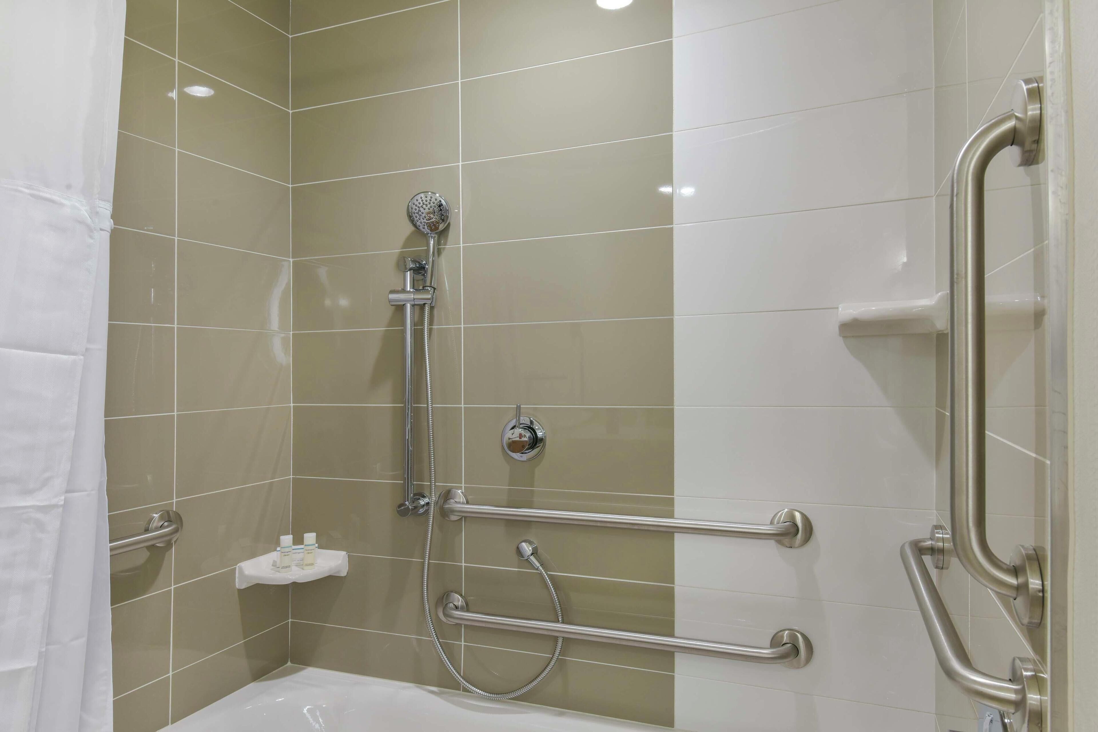 A bathroom with a shower, grab bars, and a white bathtub.