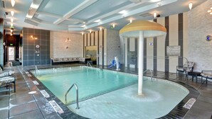 Ein überdachter Pool mit einem zentralen Wasserspiel, Sitzbereichen und einem modernen Deckenstil.