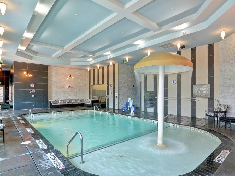 An indoor swimming pool with a central water feature, seating areas, and a modern ceiling design.