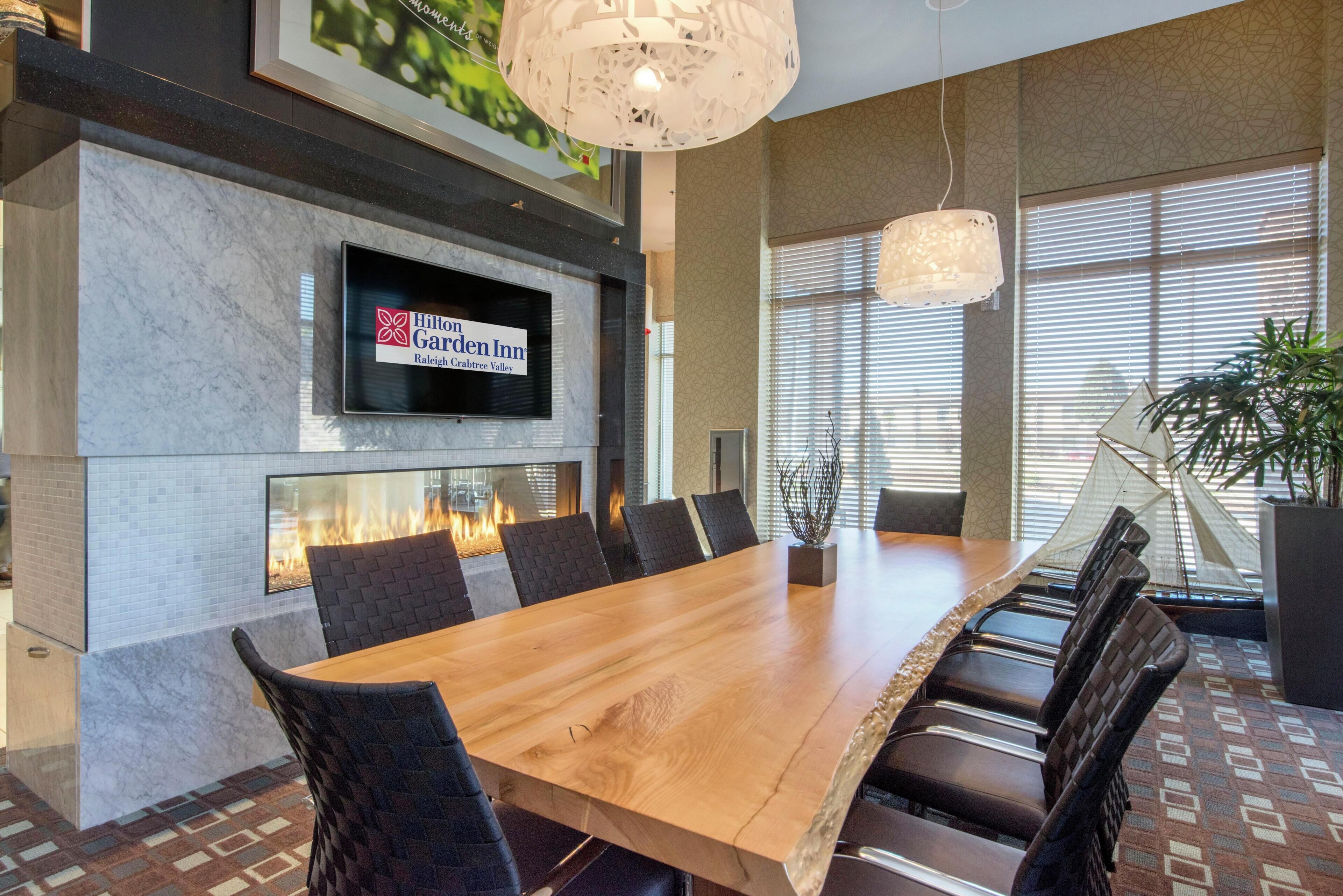 A conference room with a long table, chairs, a fireplace, a TV, and a plant.
