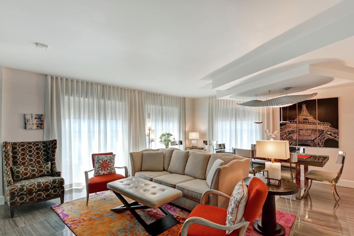 A modern living room with a sectional sofa, a patterned armchair, a small table with a lamp, and a decorative wall piece.