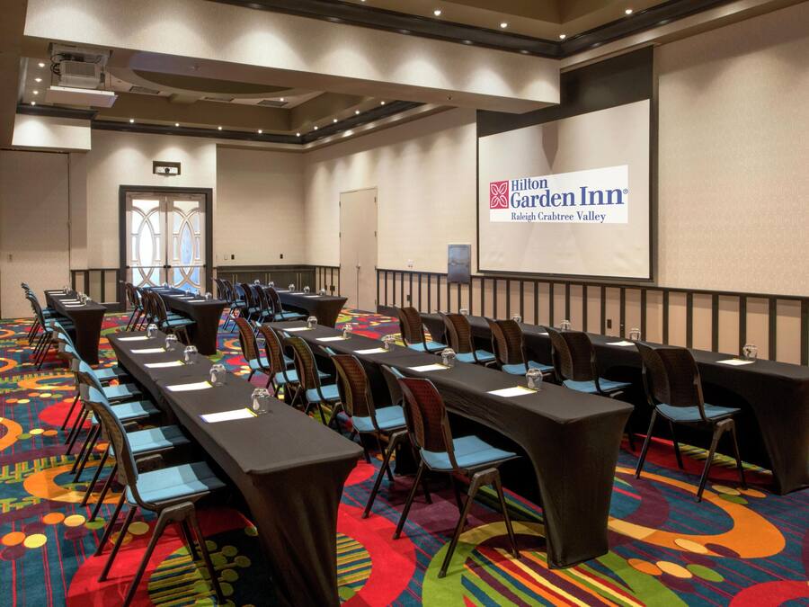 Ein Konferenzraum im Hilton Garden Inn mit langen Tischen, Stühlen und einer Projektionsleinwand, die den Namen des Hotels zeigt.