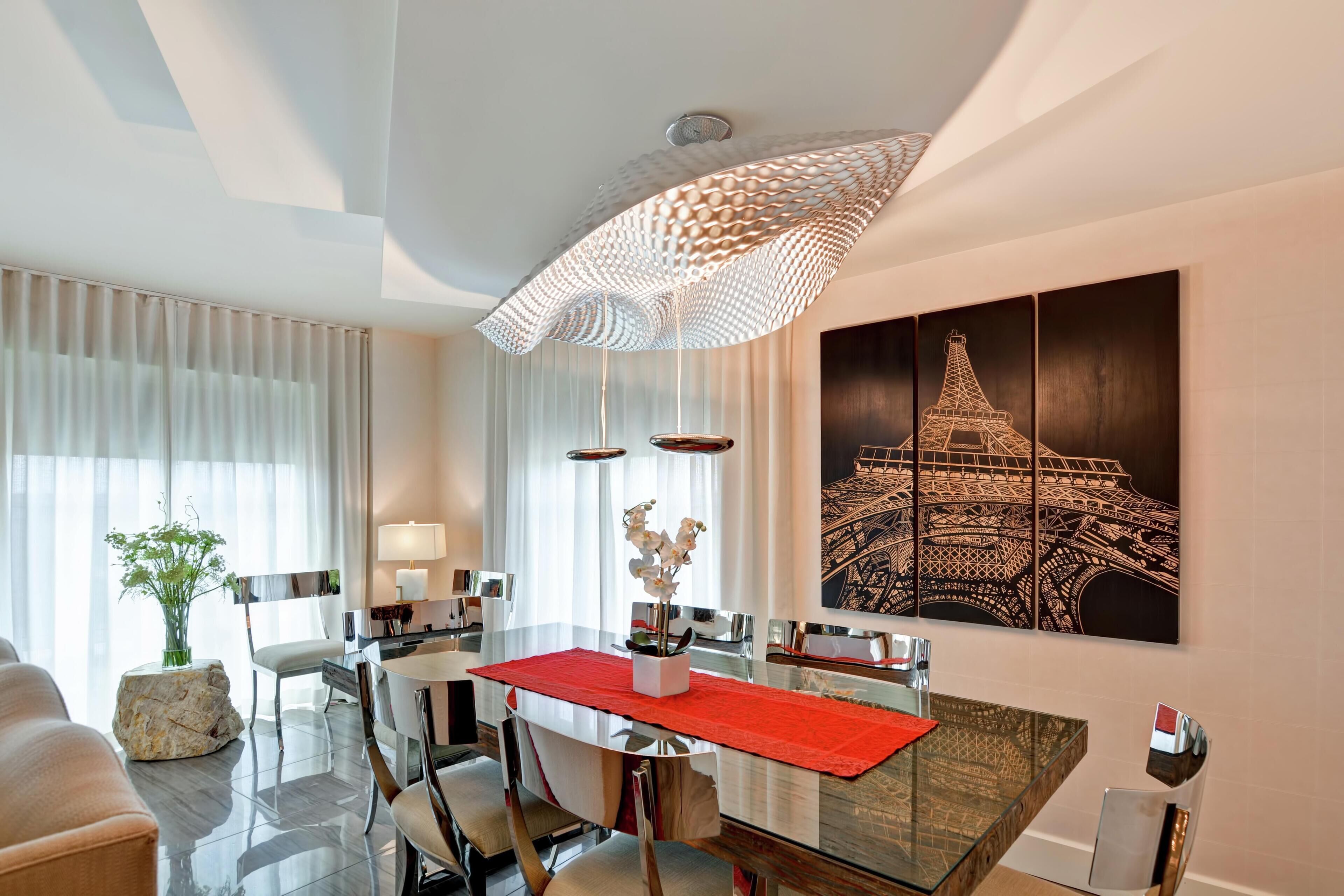 A modern dining area with a glass table, red runner, and a large Eiffel Tower painting on the wall.