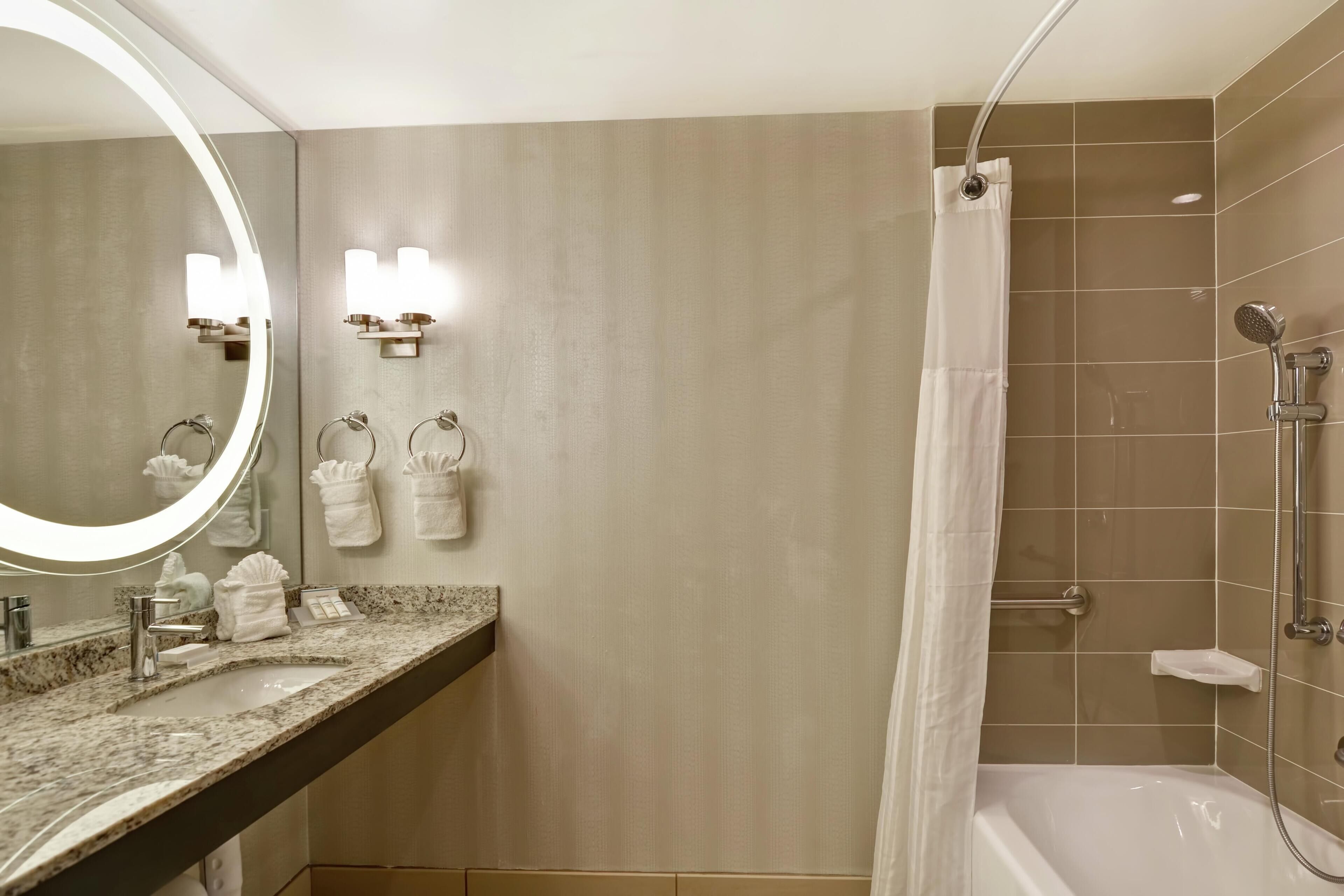 Une salle de bain équipée d’un lavabo, d’un miroir, d’un porte-serviettes, d’une douche et d’une baignoire.