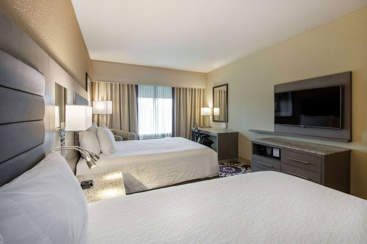A hotel room with two beds, a desk, a television, and a window with curtains.