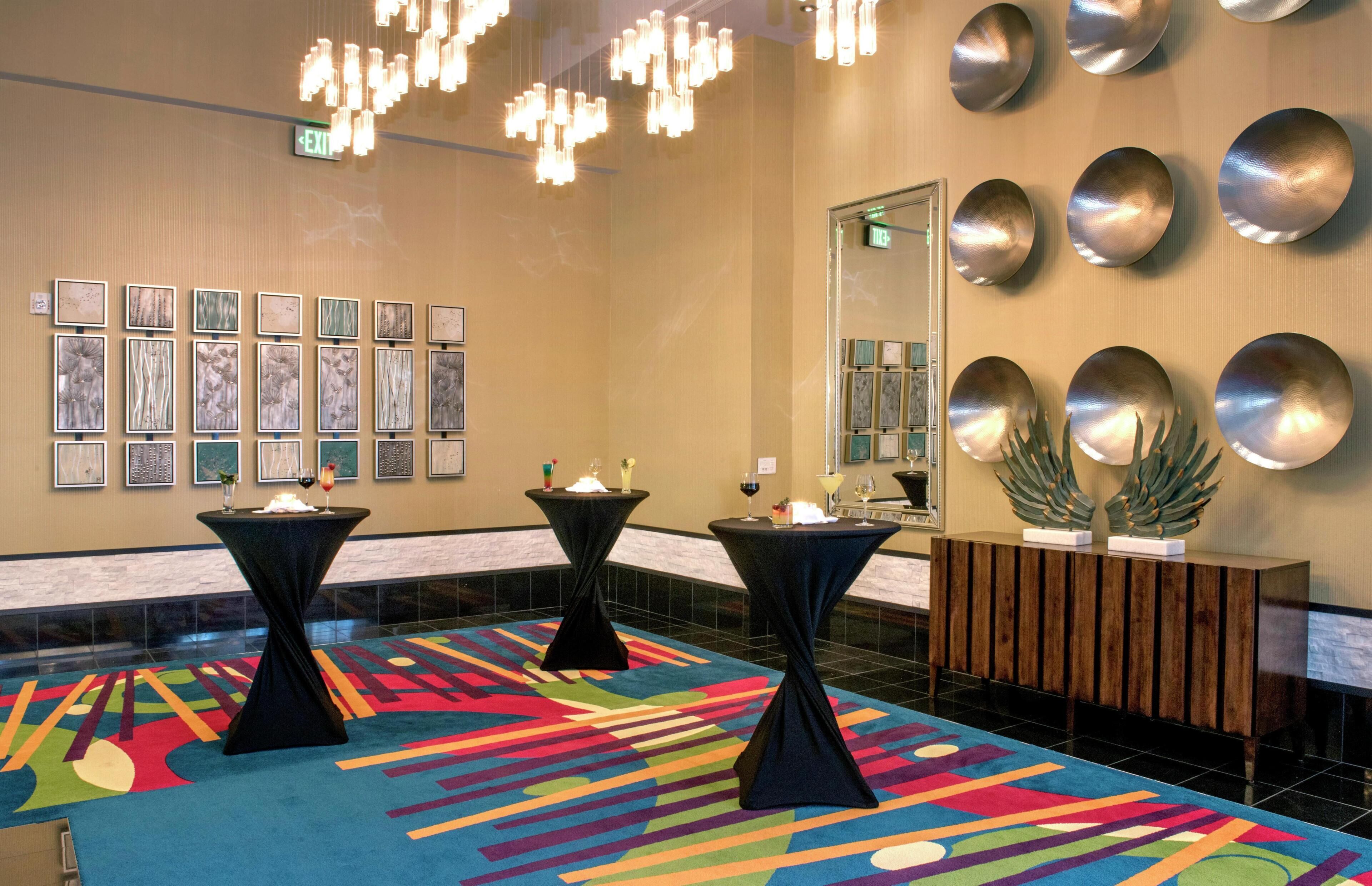 A lobby with a colorful carpet, black tables with candles, wall-mounted mirrors, and a wooden console.