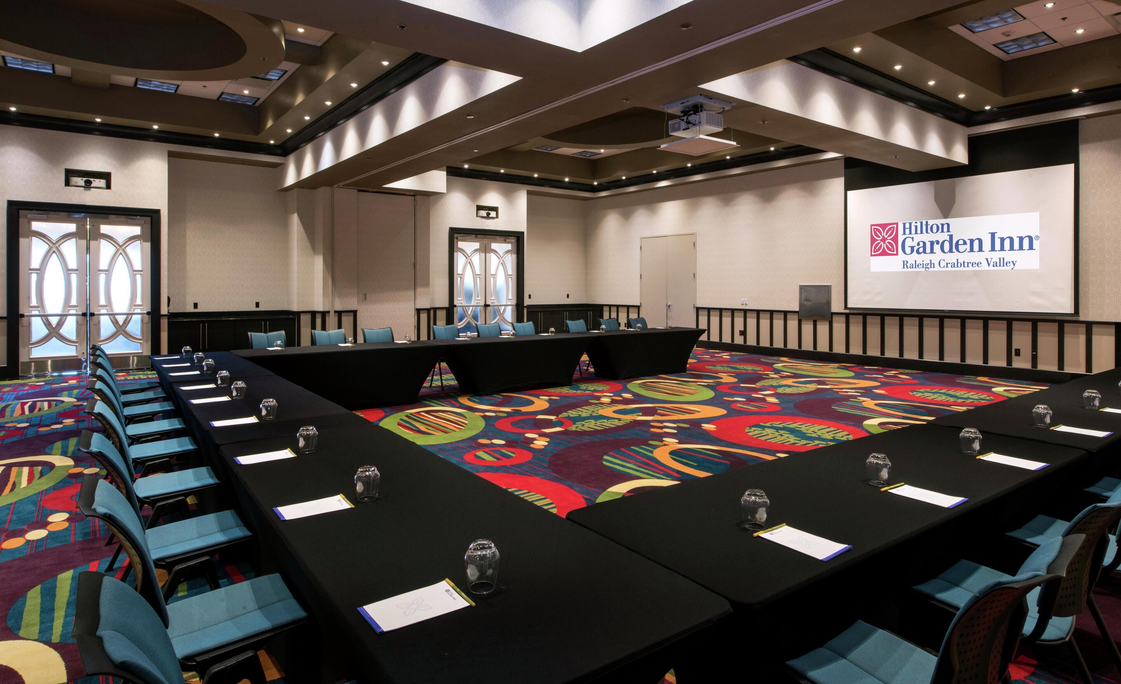A conference room with a long table, chairs, a projector screen, and a carpeted floor.