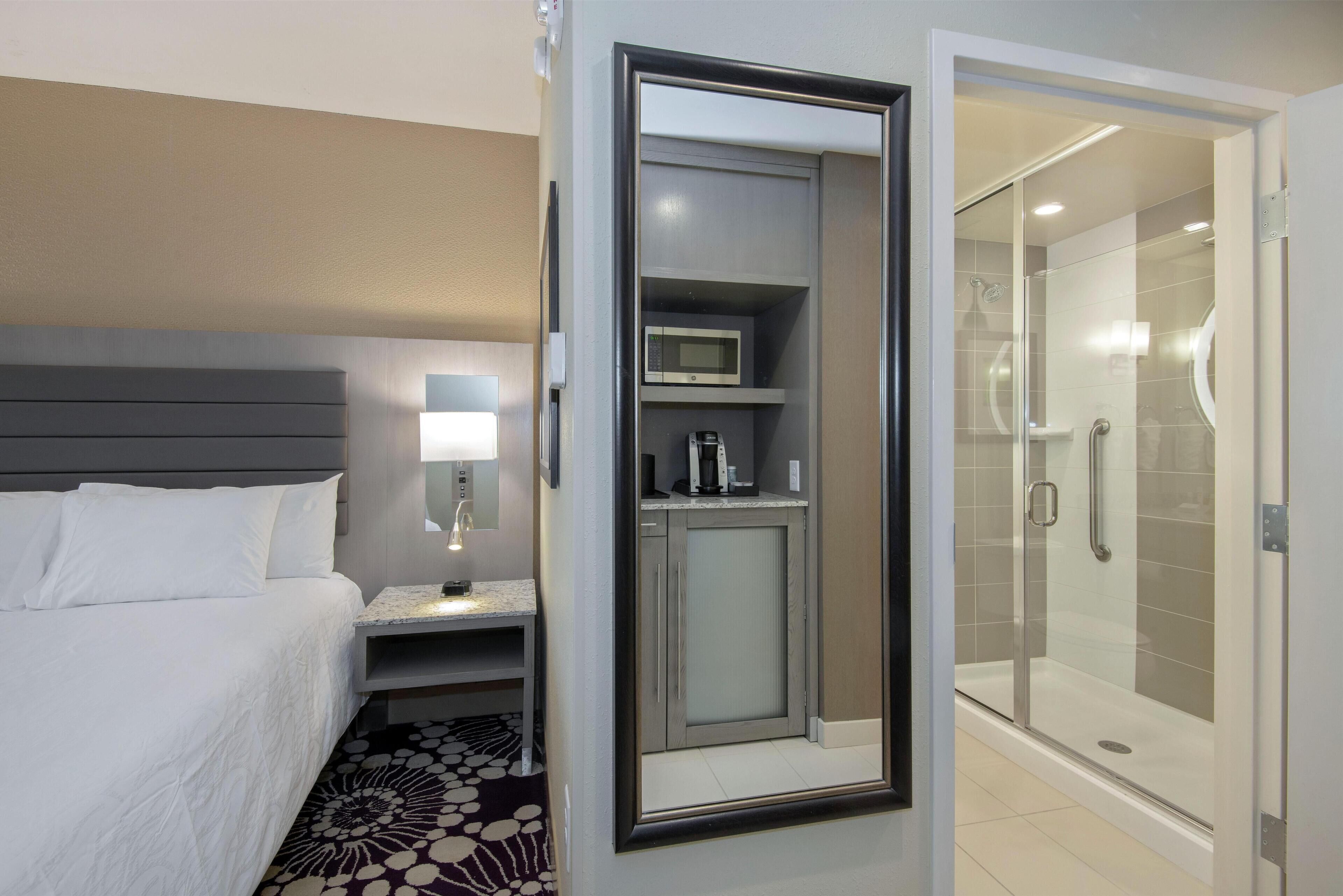 Habitación de hotel con cama, mesita de noche con lámpara, microondas, armario y zona de ducha.