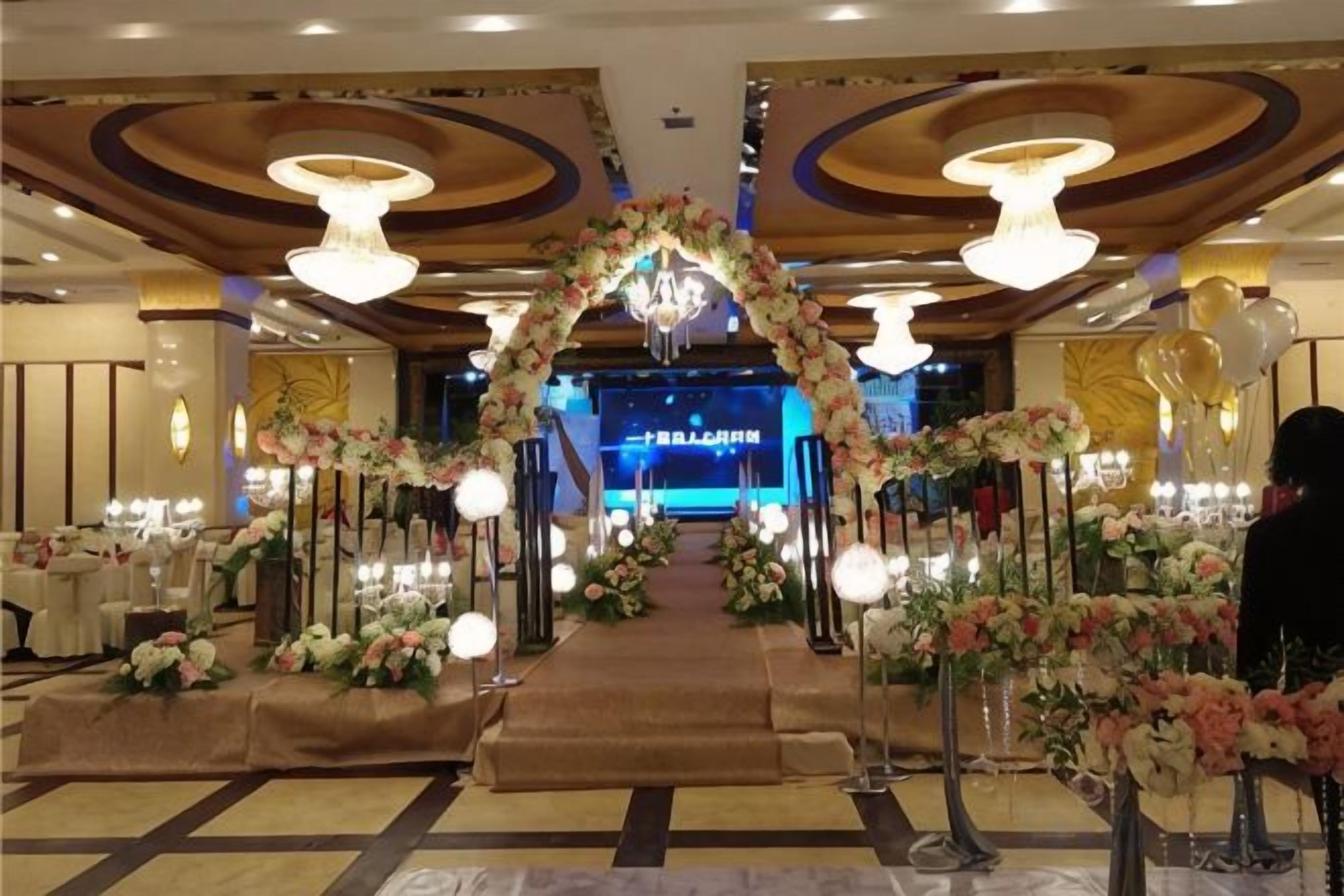 Un vestíbulo de hotel con un arco floral, mesas redondas y un escenario al fondo.