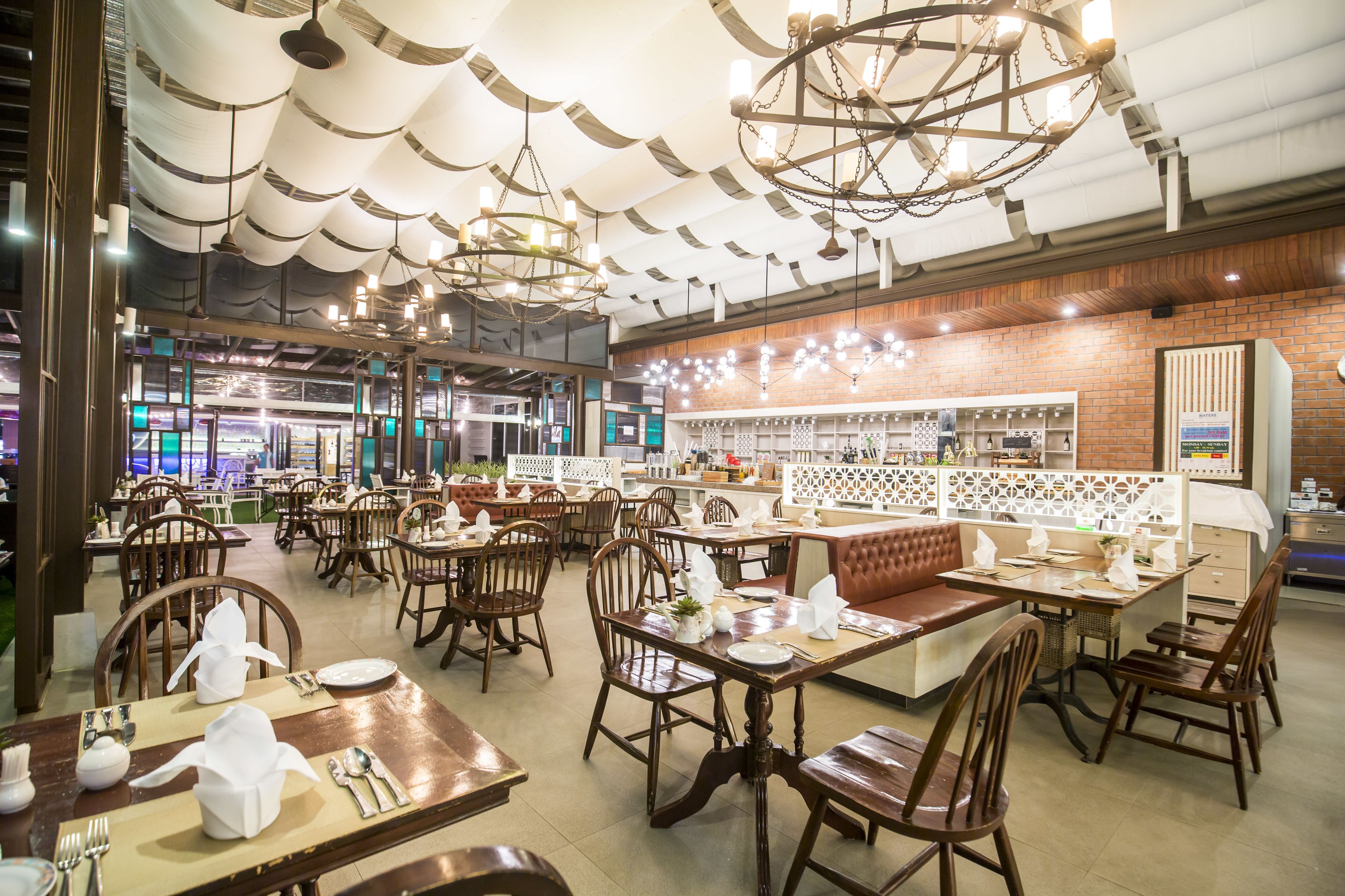 A restaurant with multiple dining tables and booths, wooden chairs, and hanging chandeliers.