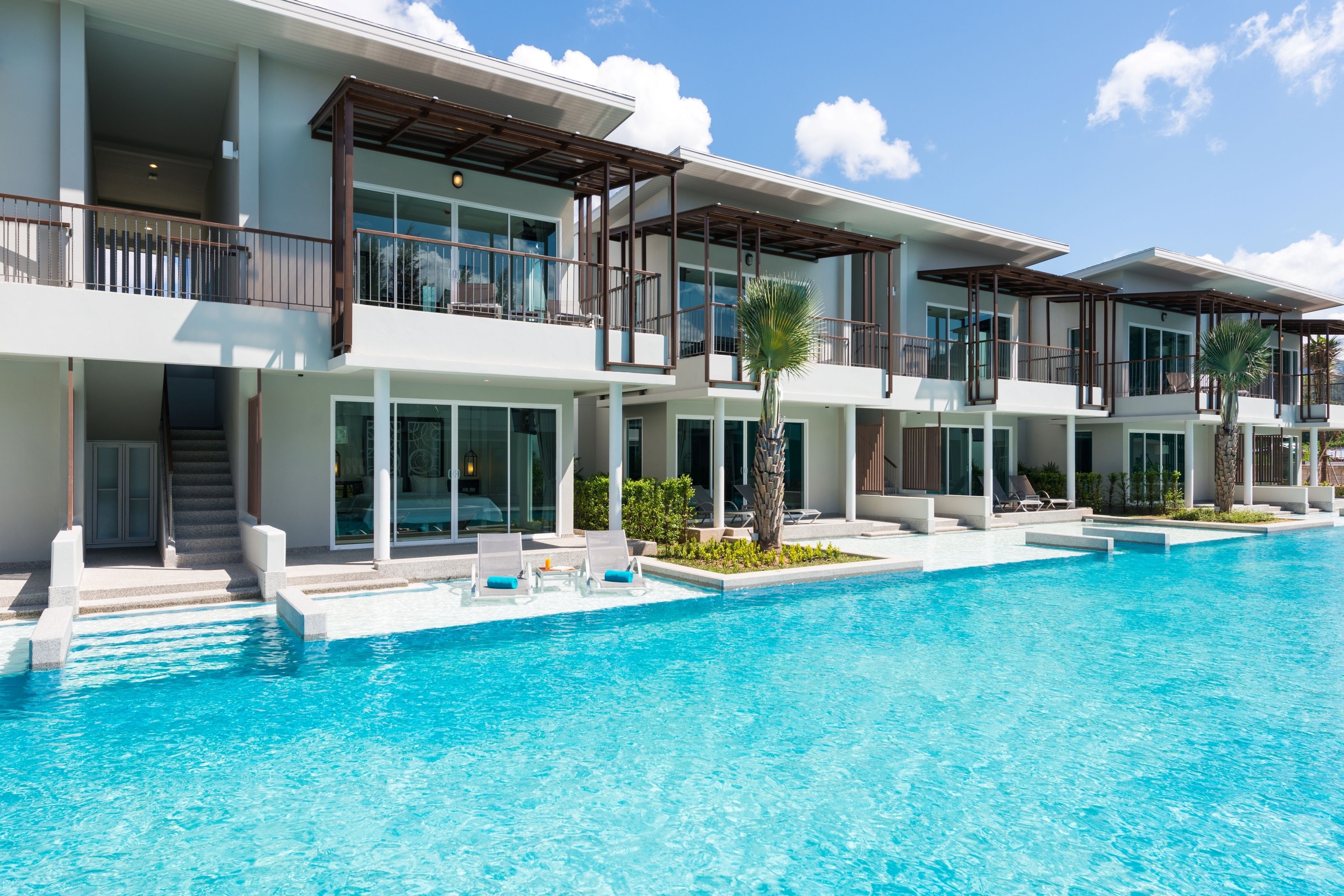 Un hotel moderno con una piscina grande, varios balcones y zonas de estar al aire libre.