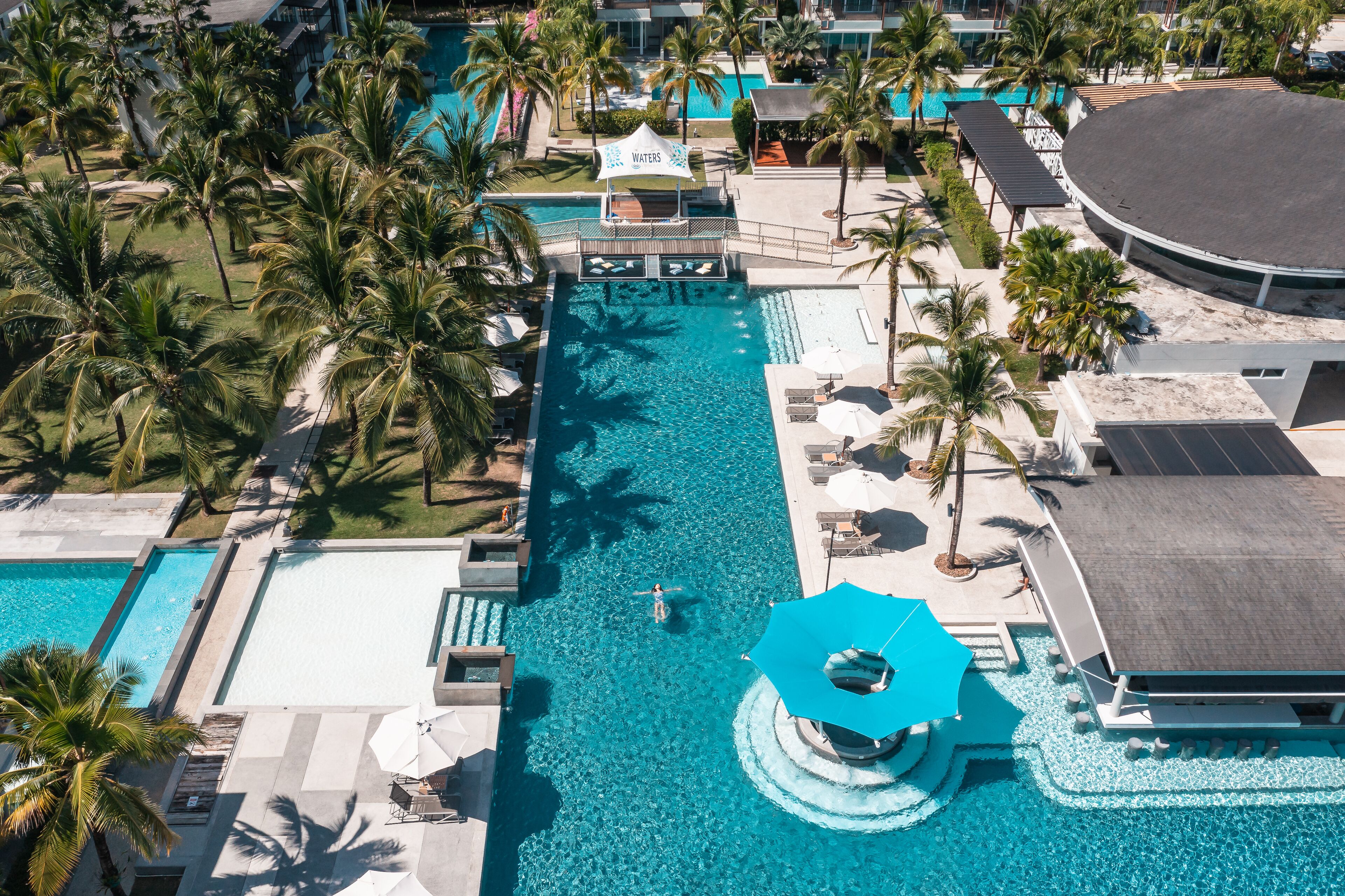 A large swimming pool with a water slide, surrounded by palm trees and lounge chairs.