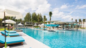 Une piscine entourée de palmiers et de bâtiments modernes, avec des chaises longues et des parasols.